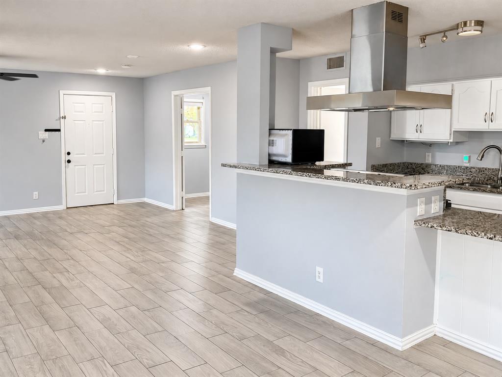 Kitchen featuring stone-finish countertops, stainless steel chimney-style range hood, white cabinetry, and wood-finish flooring throughout