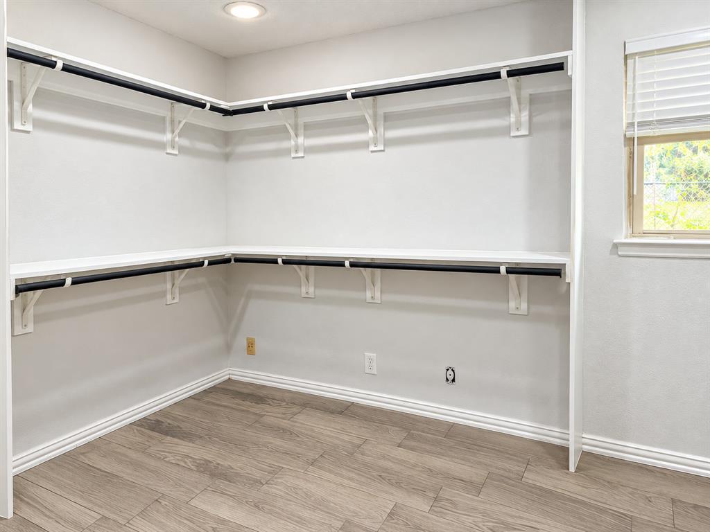 Storage space featuring white built-in shelving, dark metal garment rods, wood-finish flooring, recessed ceiling lighting, and an operable window with horizontal blinds