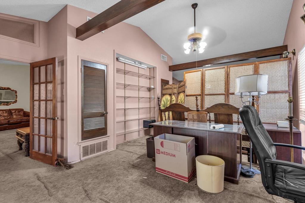 Vaulted ceiling with exposed wood beams, built-in shelving, wood-finish louvered door, and a glass-paneled entry door