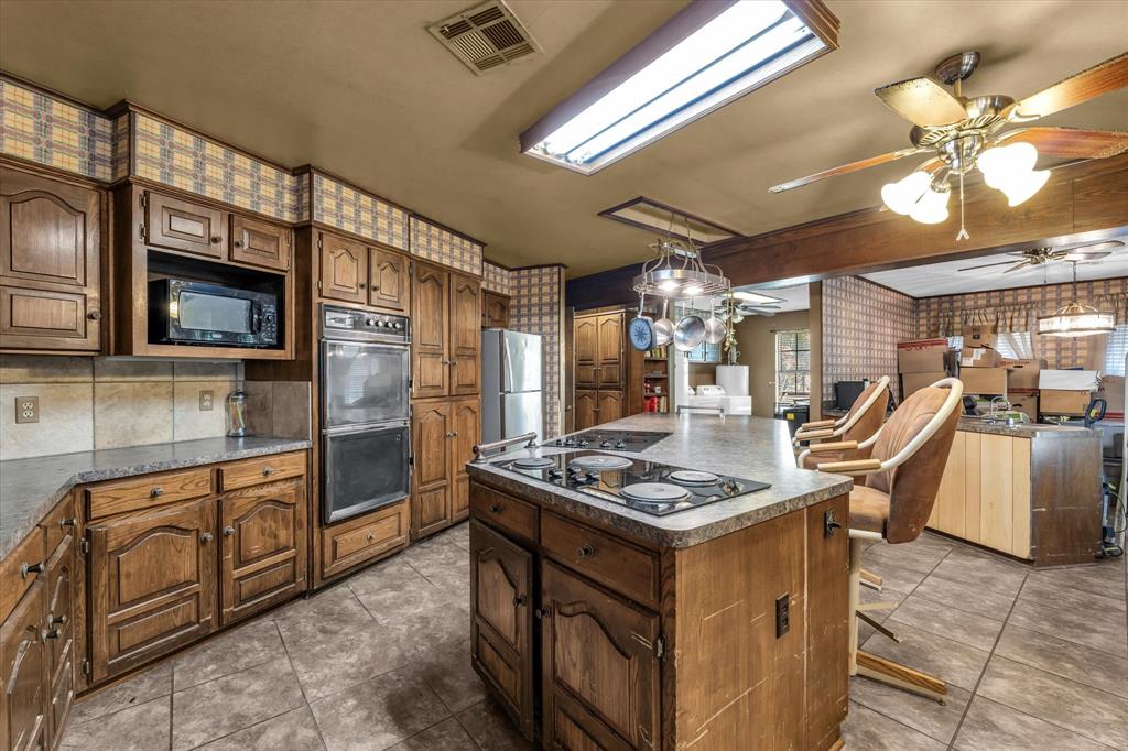 Kitchen featuring wood cabinetry, an integrated double oven, a center island with a cooktop, and tile flooring