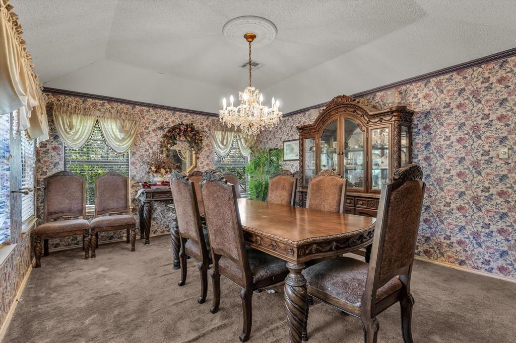 Vaulted ceiling with a central chandelier, patterned wallpaper, and carpeted flooring