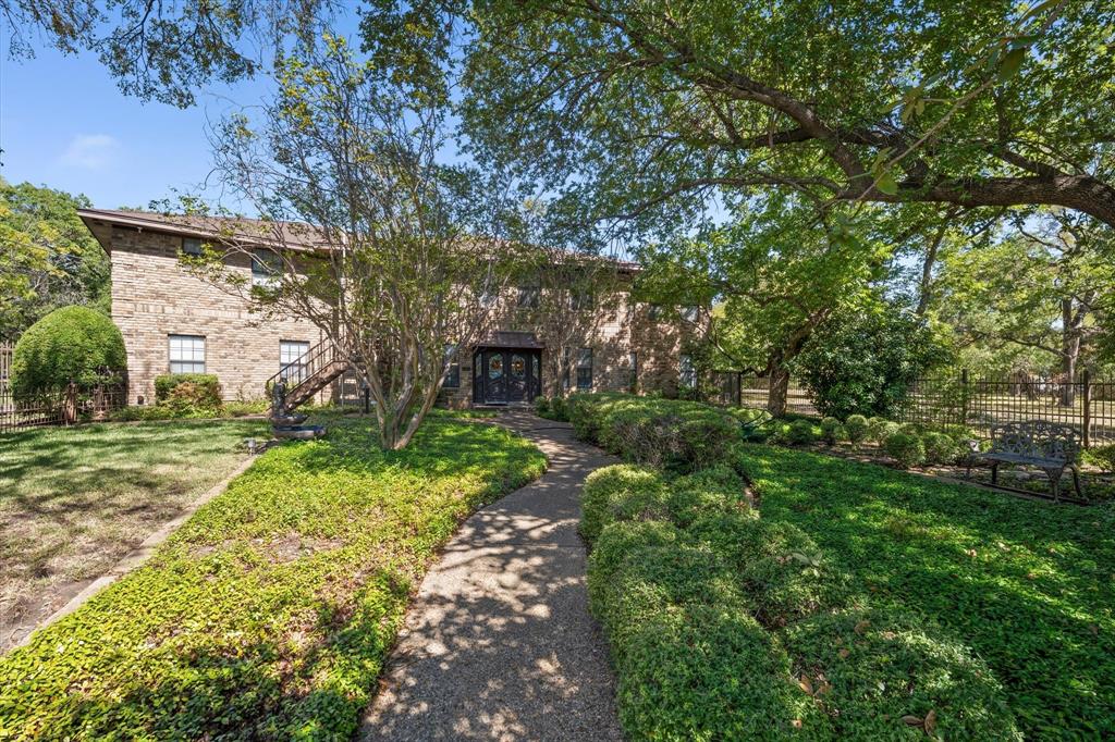 Brick exterior with a gabled roofline, featuring a stone-paved walkway, mature trees, and manicured landscaping