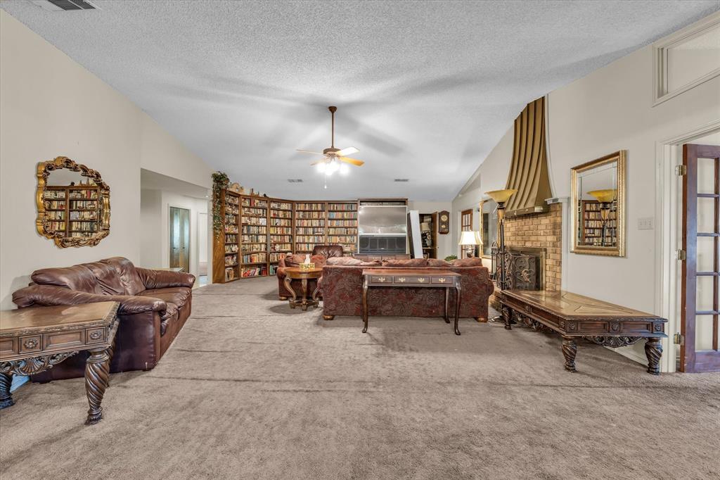 Vaulted ceilings, a built-in curved bookshelf, a brick fireplace with a decorative mantel, and a ceiling fan create a spacious interior