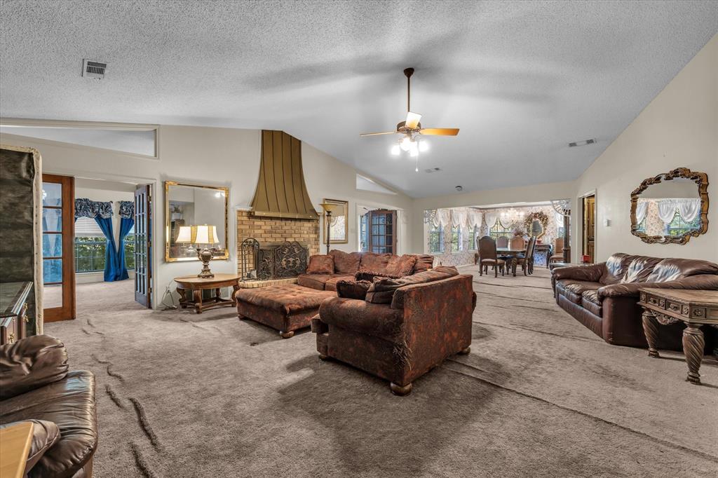 Spacious living area featuring a brick fireplace with a custom metal hood, vaulted ceilings, and a ceiling fan