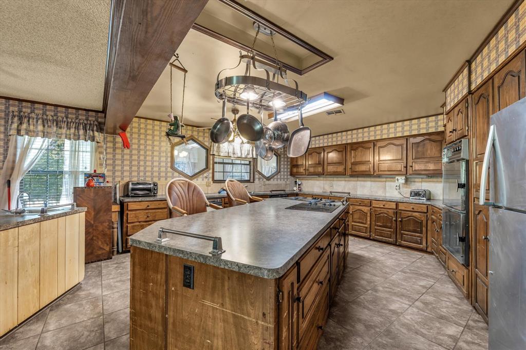Spacious kitchen with a large central island, integrated cooktop, wood cabinetry, and a pot rack
