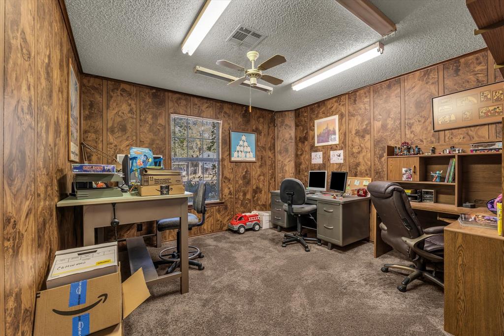 Textured wood paneling, carpeted flooring, ceiling fan, natural light window, built-in shelving