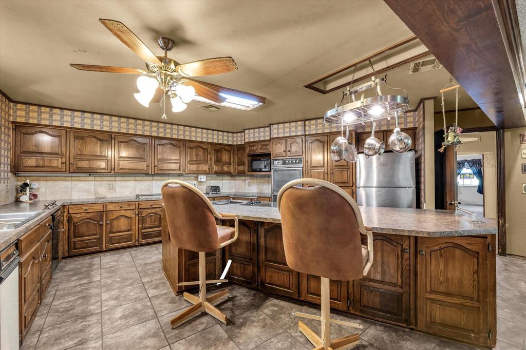 Kitchen featuring wood cabinetry, tile flooring, stone-finish countertops, and a ceiling fan with integrated lighting