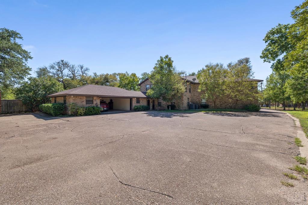 Extensive paved parking area with brick exterior structures, mature trees, and landscaping