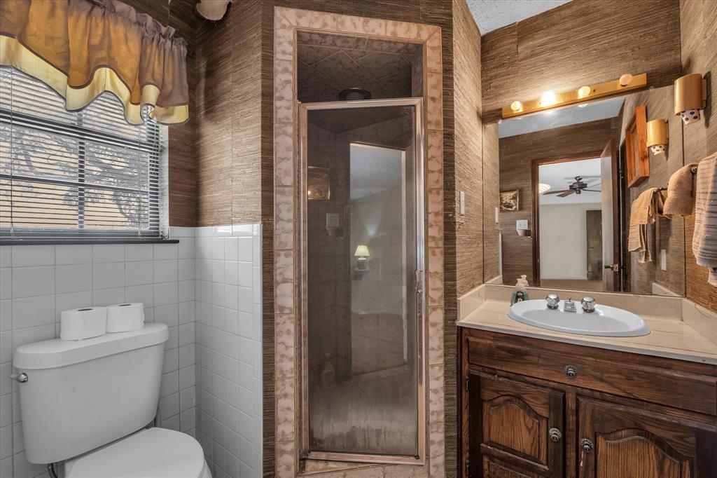 Bathroom featuring white ceramic wall tile, an enclosed shower, a single vanity with an integrated sink, and an overhead light bar