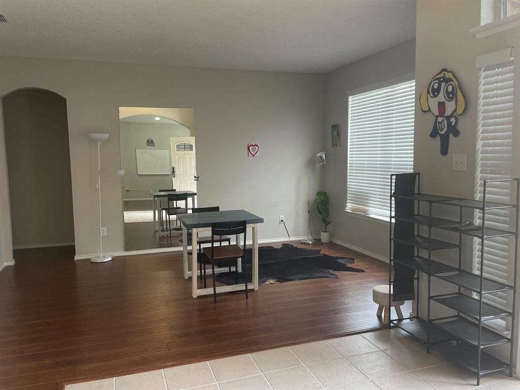 Living area featuring wood-finish flooring, neutral wall paint, arched entryways, and windows with horizontal blinds