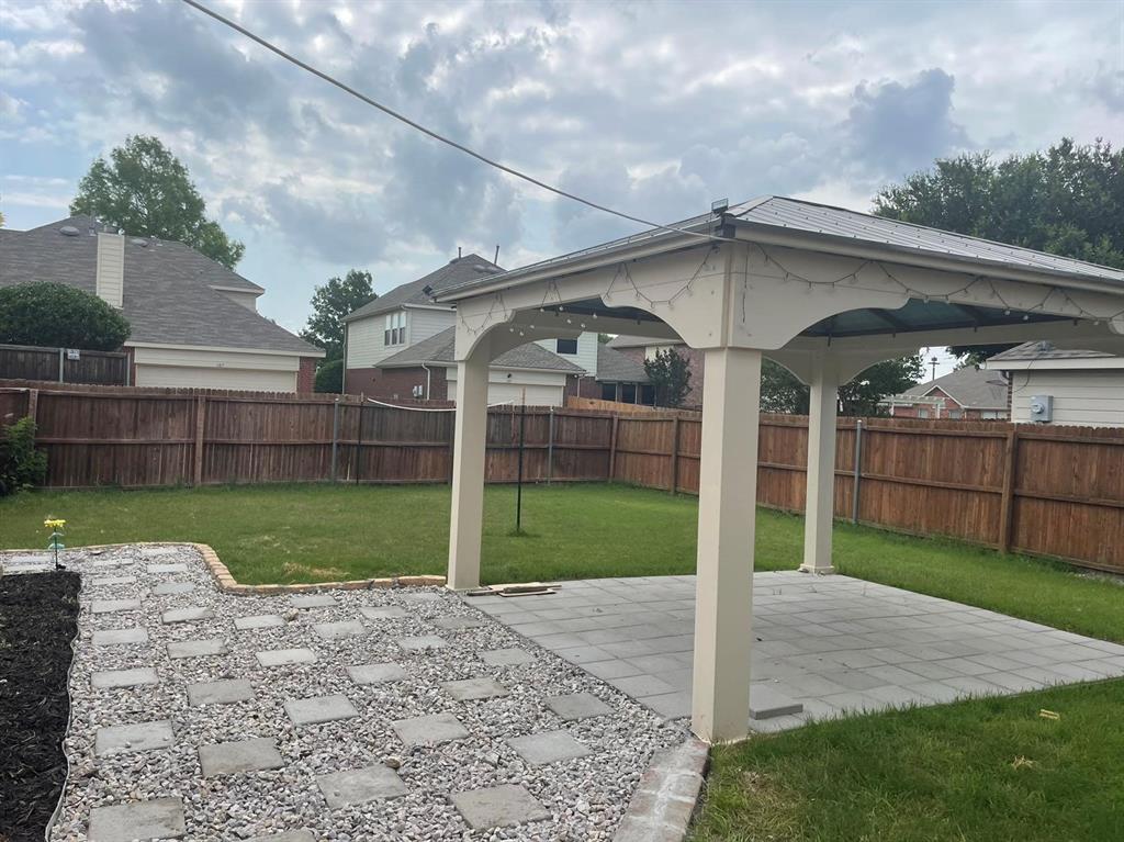 Backyard featuring a covered pavilion, paver patio, gravel pathway, and wood privacy fencing