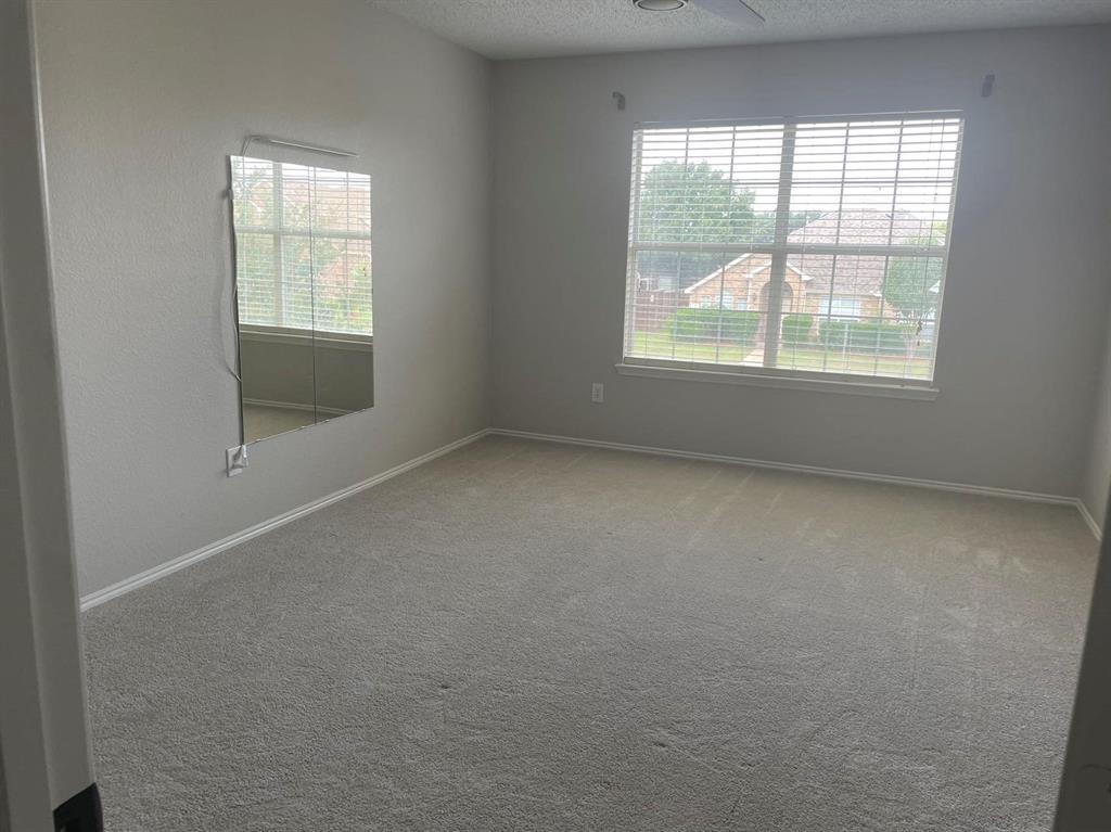 Neutral-toned carpeted flooring, large window with horizontal blinds, wall-mounted light fixture, and textured wall finish