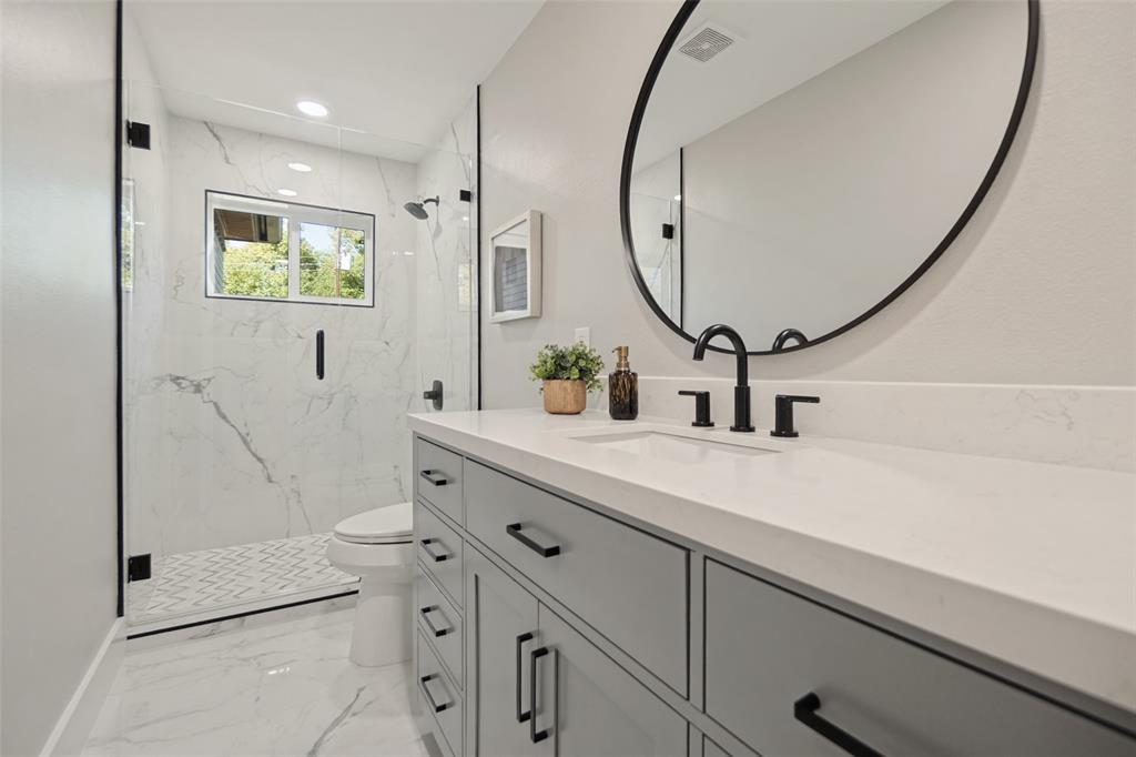 Vanity with solid surface countertop, matte black fixtures, and an oval mirror