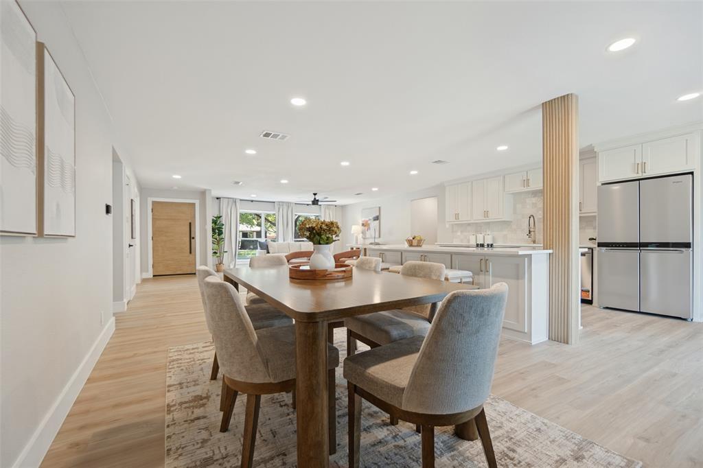 Open-concept living space with light wood-finish flooring, recessed lighting, white shaker cabinets, and stainless steel appliances