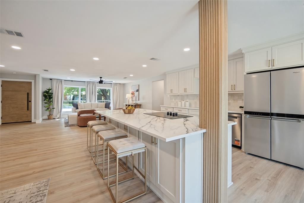 Open-concept living space featuring wood-finish flooring, a kitchen island with stone countertop, built-in cooktop, and a stainless steel refrigerator