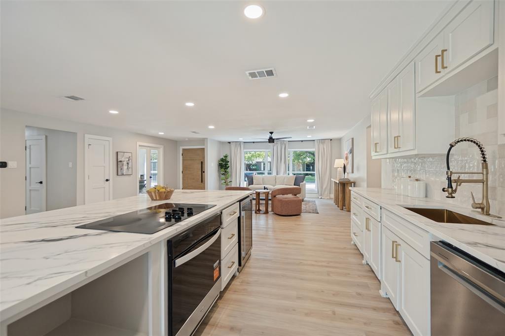 Kitchen featuring an expansive island with cooktop, white cabinetry with gold-tone hardware, stainless steel appliances, and wood-finish flooring