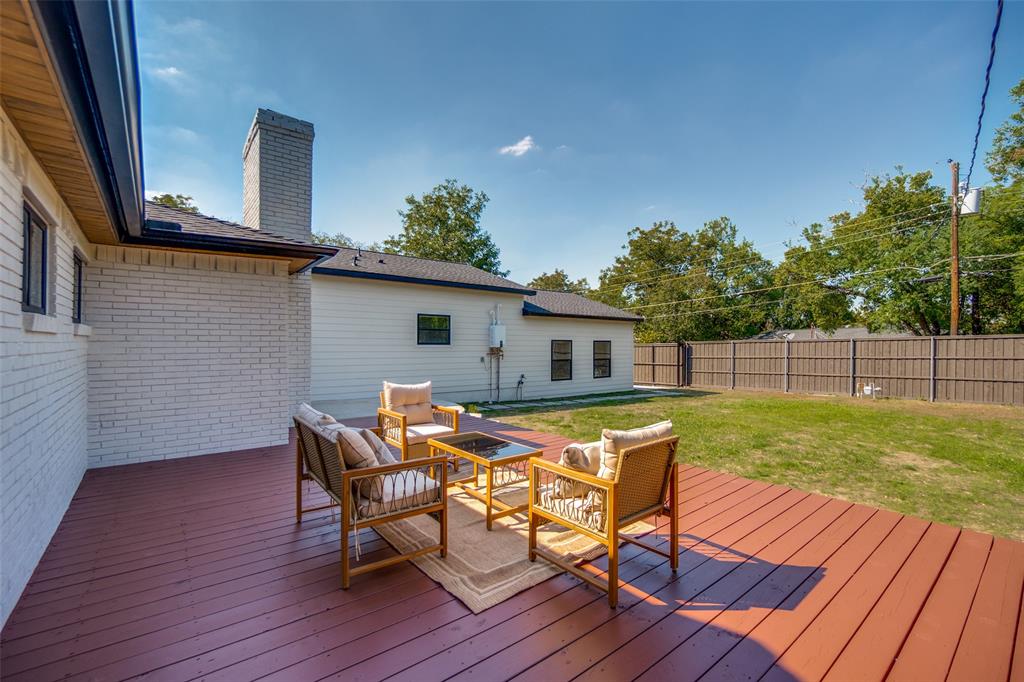 Expansive wood deck with a red-brown finish, white brick exterior, black gutters, and a gray stone chimney