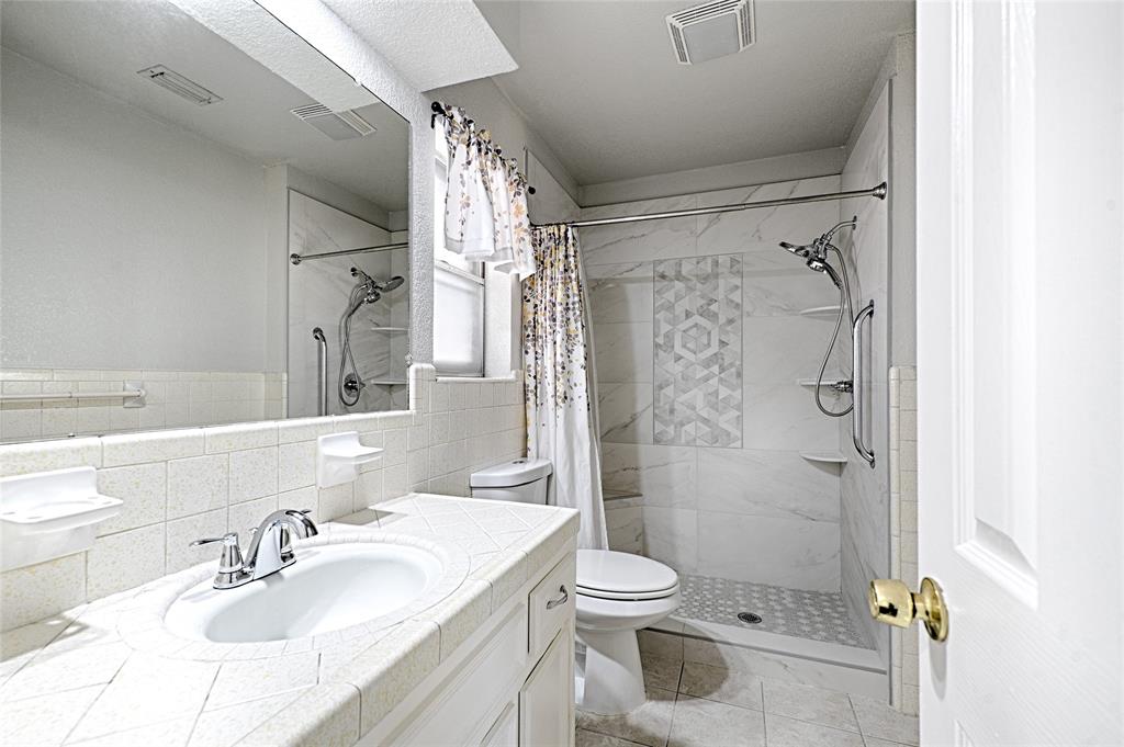 Bathroom featuring a vanity with a tile-surround countertop, integrated porcelain sink, full-width wall mirror, and a walk-in shower with decorative mosaic tile inlay and integrated shelving
