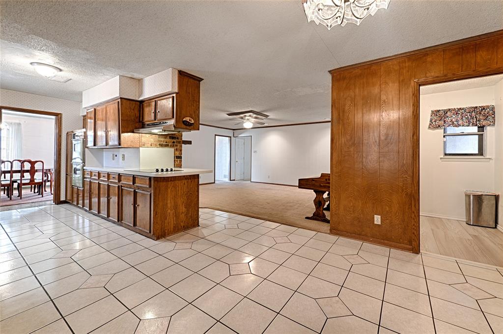 Kitchen featuring stained wood cabinetry, a built-in wall oven, a cooktop with a range hood, and tile flooring
