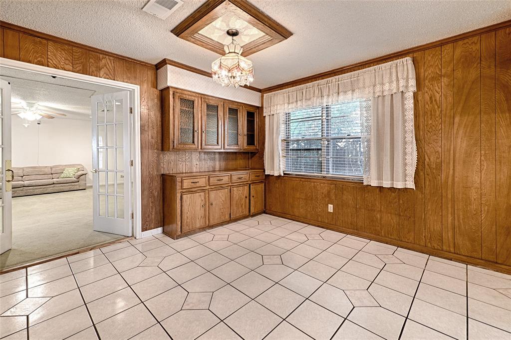 Wood-paneled walls, built-in wooden cabinetry with glass-front uppers, ceramic tile flooring, and a decorative ceiling-mounted chandelier