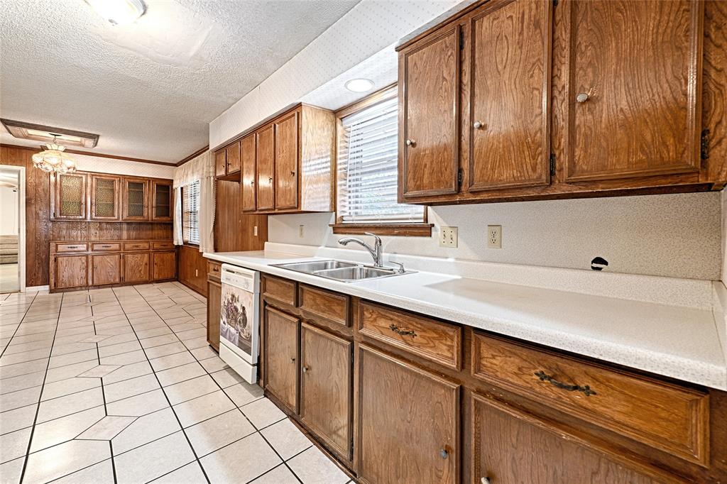 Wood-finish cabinetry, white solid-surface countertops, dual-basin stainless steel sink, ceramic tile flooring, and integrated built-in storage hutch Wood-finish cabinetry, white solid-surface countertops, dual-basin stainless steel sink, ceramic tile flooring, and integrated built-in storage hutch