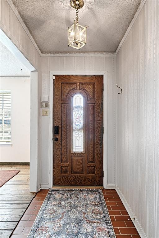 Entryway featuring a wood-finish front door with an integrated glass inlay, terra-cotta tile flooring, and a decorative ceiling medallion with a suspended lantern-style light fixture Entryway featuring a wood-finish front door with an integrated glass inlay, terra-cotta tile flooring, and a decorative ceiling medallion with a suspended lantern-style light fixture