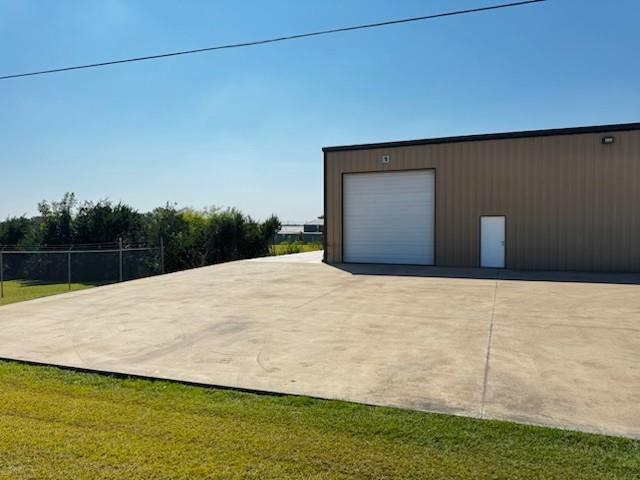 Industrial building featuring a roll-up door, personnel door, exterior lighting, and a concrete pad Industrial building featuring a roll-up door, personnel door, exterior lighting, and a concrete pad