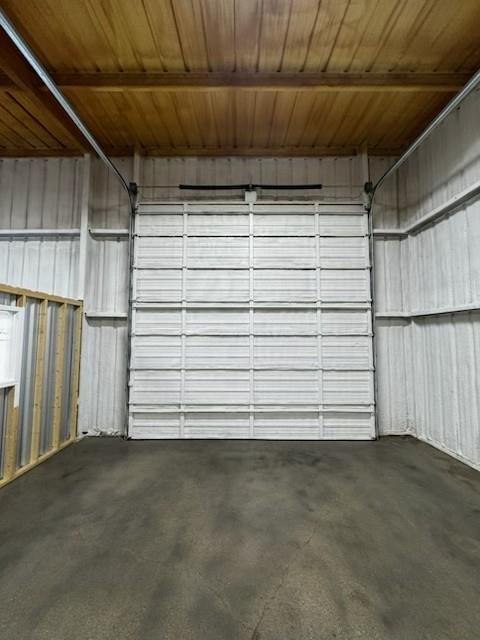 Concrete flooring with a segmented overhead door and exposed wood ceiling