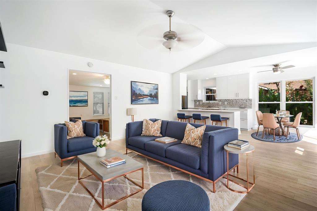 Open-concept interior featuring vaulted ceilings, wood-finish flooring, dual ceiling fans, and kitchen island with waterfall-edge countertop