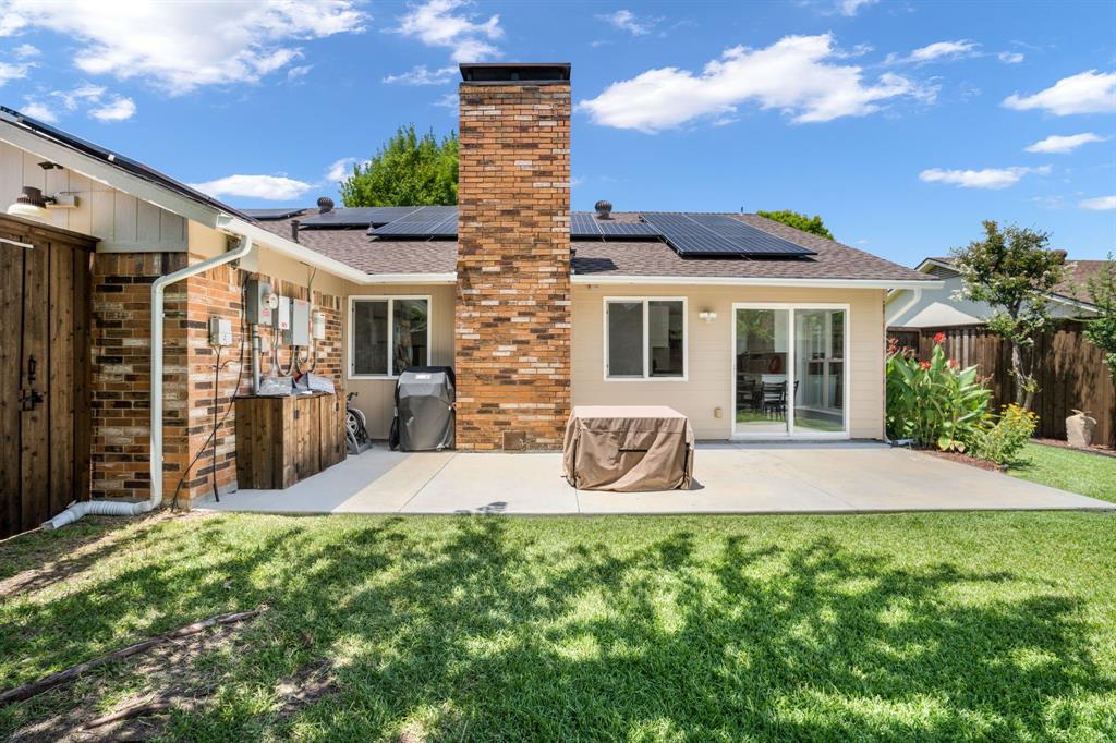 Backyard featuring a concrete patio, exterior brick chimney, roof-mounted solar panels, wood siding, and sliding glass doors