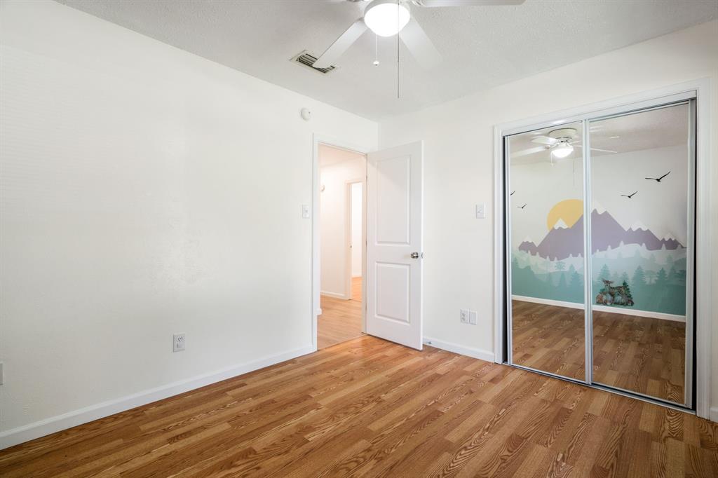 Wood-finish flooring, mirrored sliding closet doors, and a ceiling-mounted light fixture with a fan