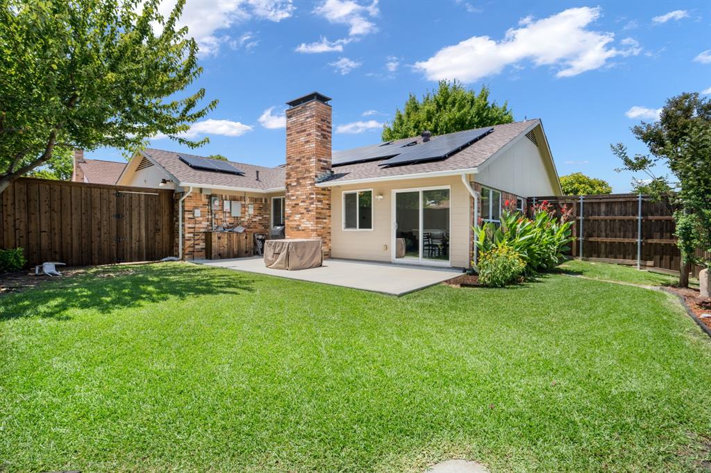 Rear exterior featuring a concrete patio, brick chimney, solar panels, and wood fencing