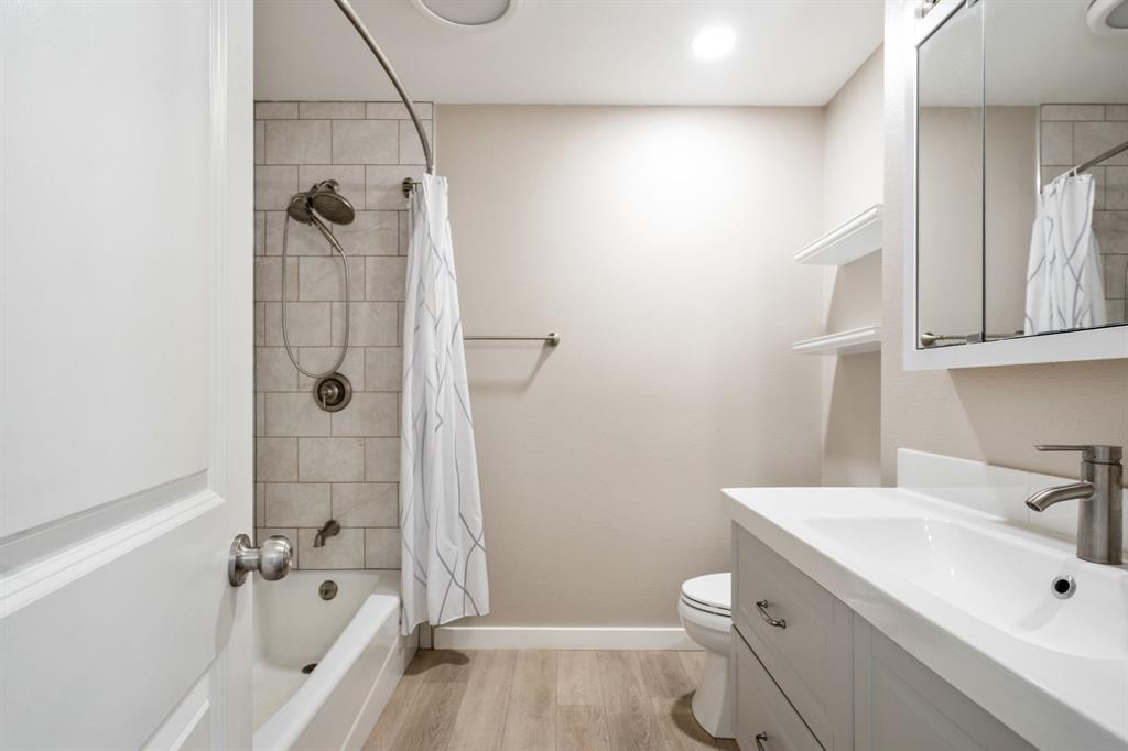 Tub and shower combination with subway tile surround, single vanity with integrated sink, wood-finish flooring, and recessed lighting