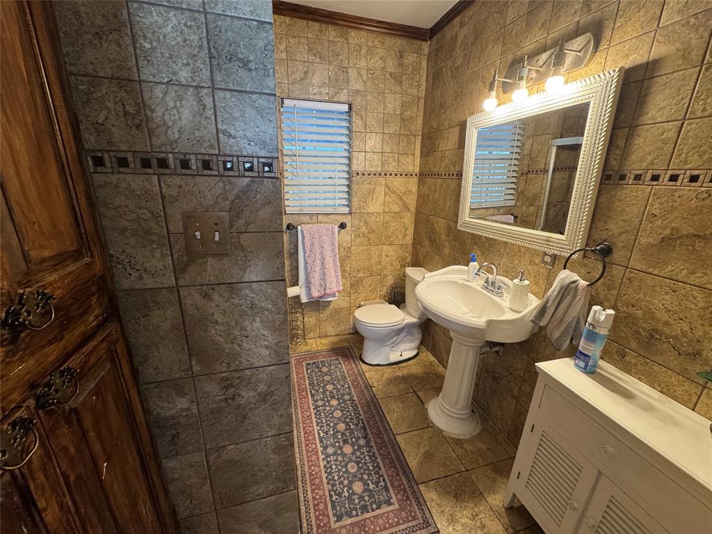 Full bathroom with tile walls, tile patterned flooring, a shower, and ornamental molding Full bathroom with tile walls, tile patterned flooring, a shower, and ornamental molding
