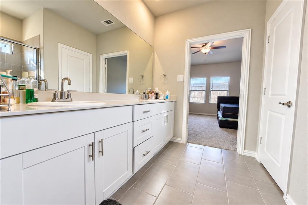 Dual vanity with white cabinetry and brushed nickel hardware, expansive wall-mounted mirror, and tile flooring