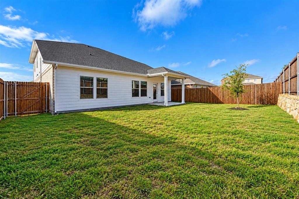 Expansive backyard with a covered patio, manicured lawn, and privacy fencing