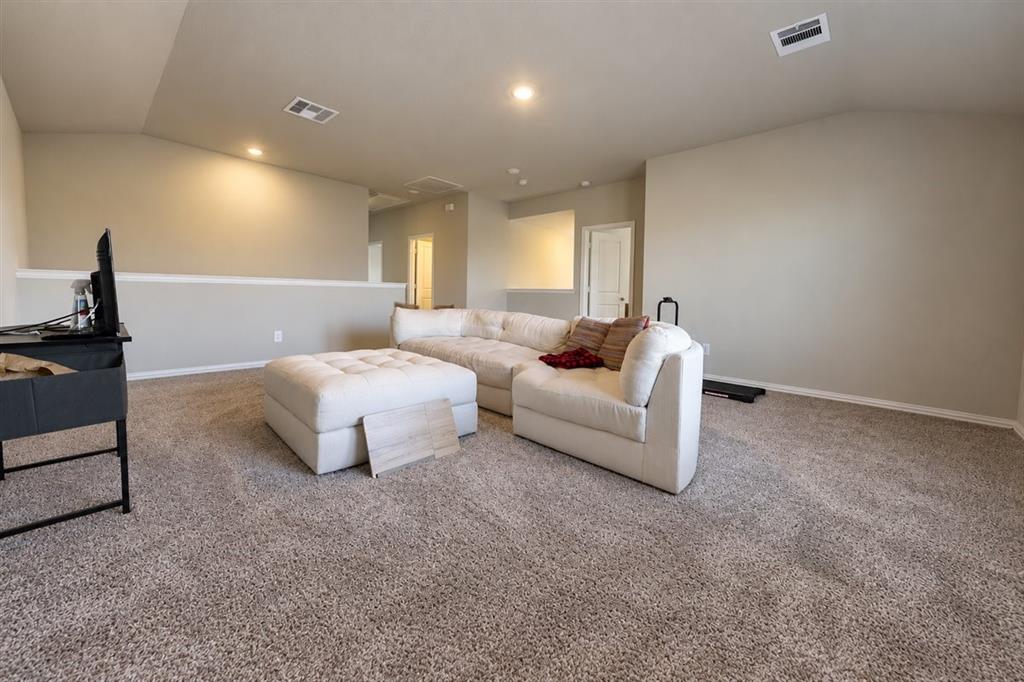 Spacious carpeted room featuring vaulted ceilings, recessed lighting, and a neutral color palette