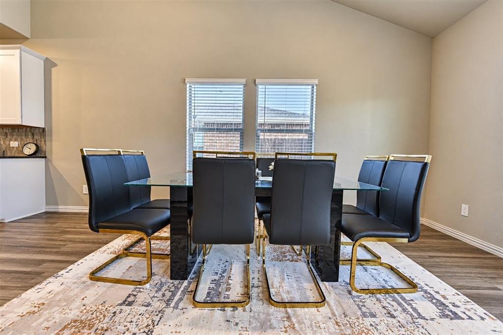 Vaulted ceilings, wood-finish flooring, white cabinetry, tiled backsplash, and natural light
