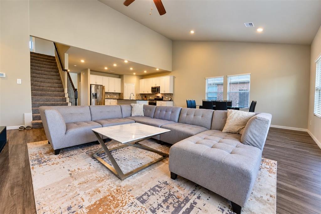 Vaulted ceiling, recessed lighting, wood-finish flooring, kitchen with stainless steel appliances, and a carpeted staircase with dark wood handrails