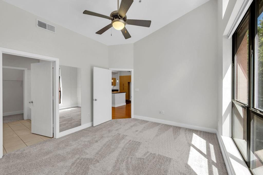 Grey carpet flooring with a ceiling fan, vaulted ceiling, and large windows