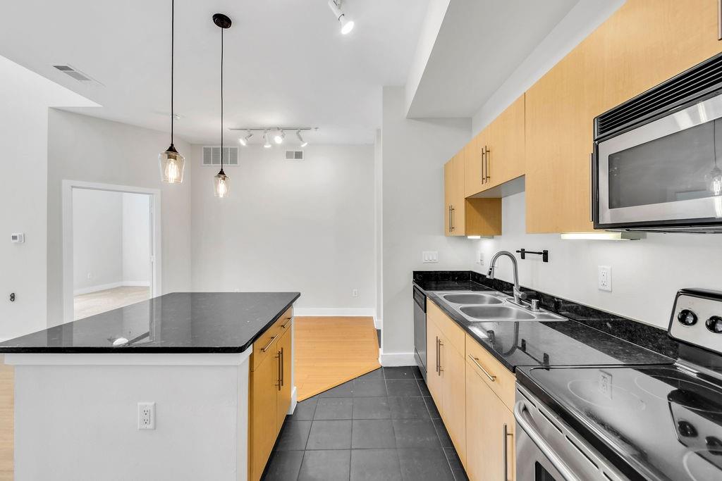 Modern kitchen featuring light wood-finish cabinetry, dark stone countertops, stainless steel appliances, and a built-in microwave