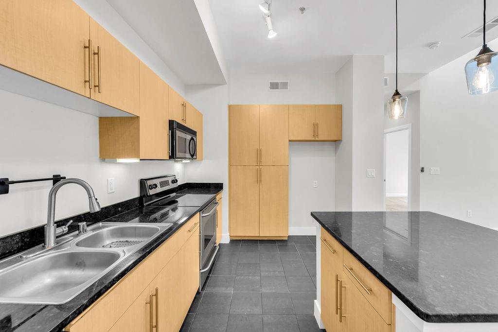 Kitchen featuring dark stone countertops, light wood-finish cabinetry, stainless steel appliances, and dark tile flooring