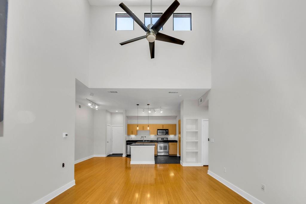 Soaring ceilings with transom windows, wood-finish flooring, modern ceiling fan, built-in shelving, and contemporary kitchen with stainless steel appliances