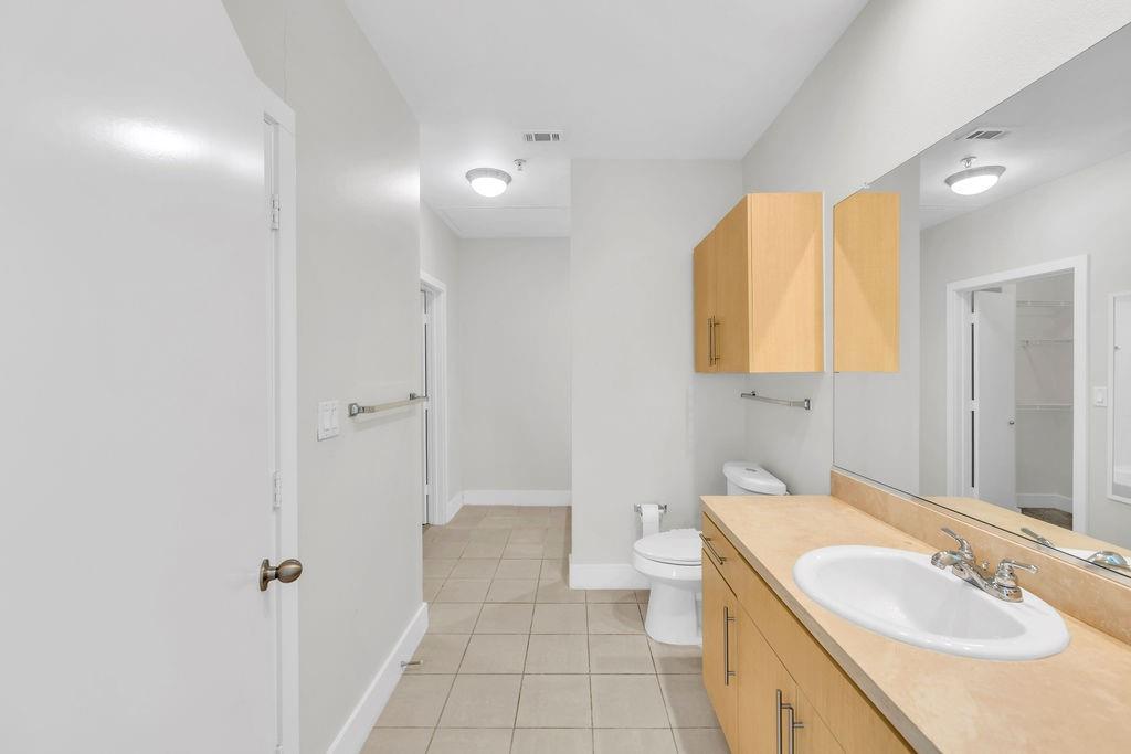Full-length vanity mirror, ample wood-finish cabinetry, tile flooring, and recessed lighting