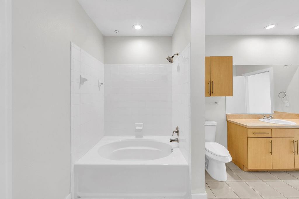 Soaking tub with tile surround, wood-finish vanity with countertop, integrated sink, and wall-mounted mirror