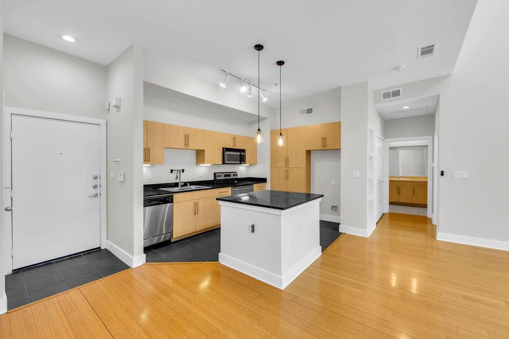 Open-concept kitchen featuring wood-finish cabinetry, stainless steel appliances, a center island with a dark countertop, and pendant lighting