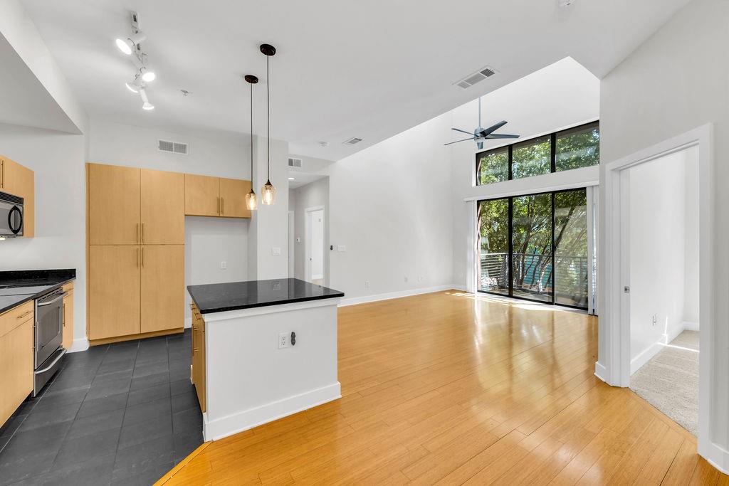 Open-concept living area with high ceilings, wood-finish flooring, a kitchen island with a dark countertop, and large windows with a sliding glass door