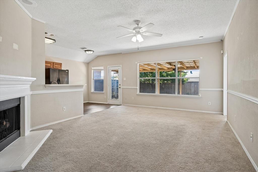 Spacious living area featuring a fireplace, vaulted ceiling, ceiling fan with integrated lighting, and direct outdoor access