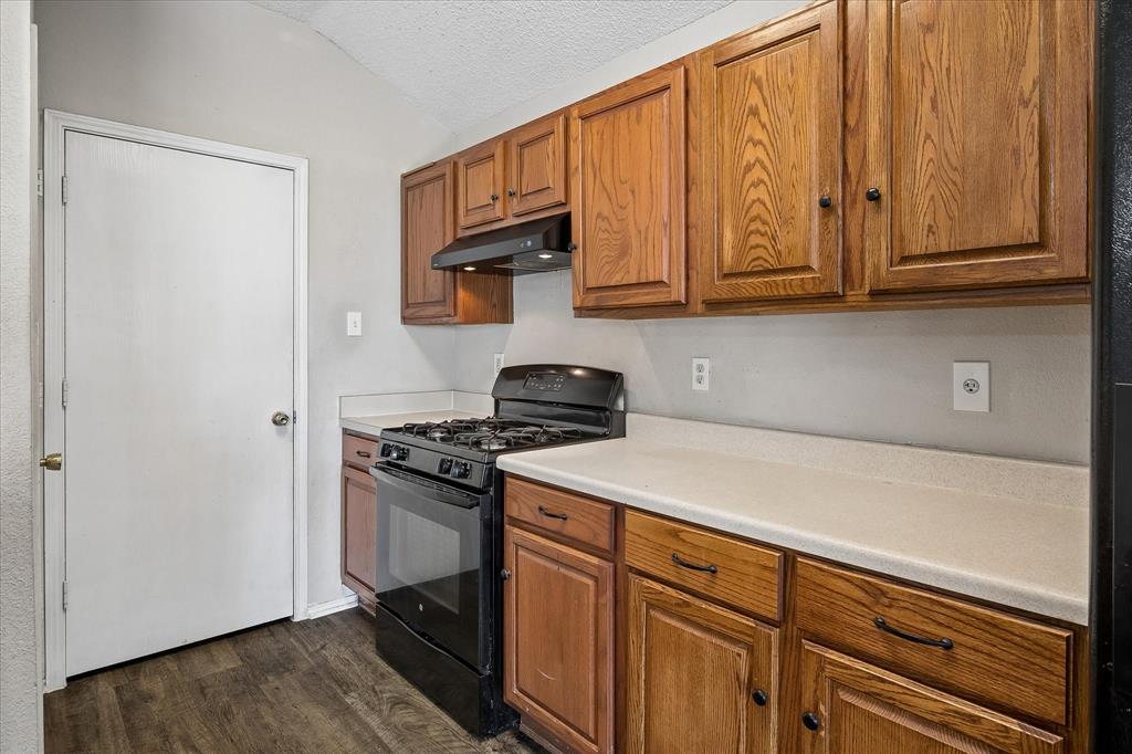Kitchen featuring wood-finish cabinetry, solid surface countertops, a black gas range, and wood-finish flooring