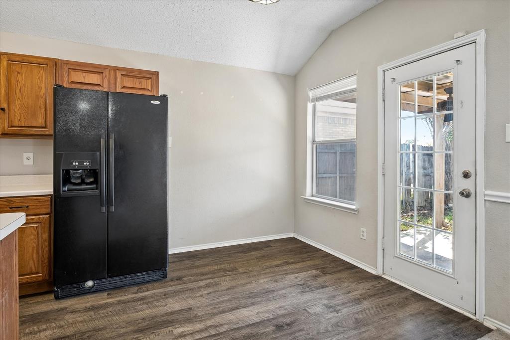 Wood-finish flooring with vaulted ceiling, featuring a side-by-side refrigerator, wood cabinetry, and a full-light door